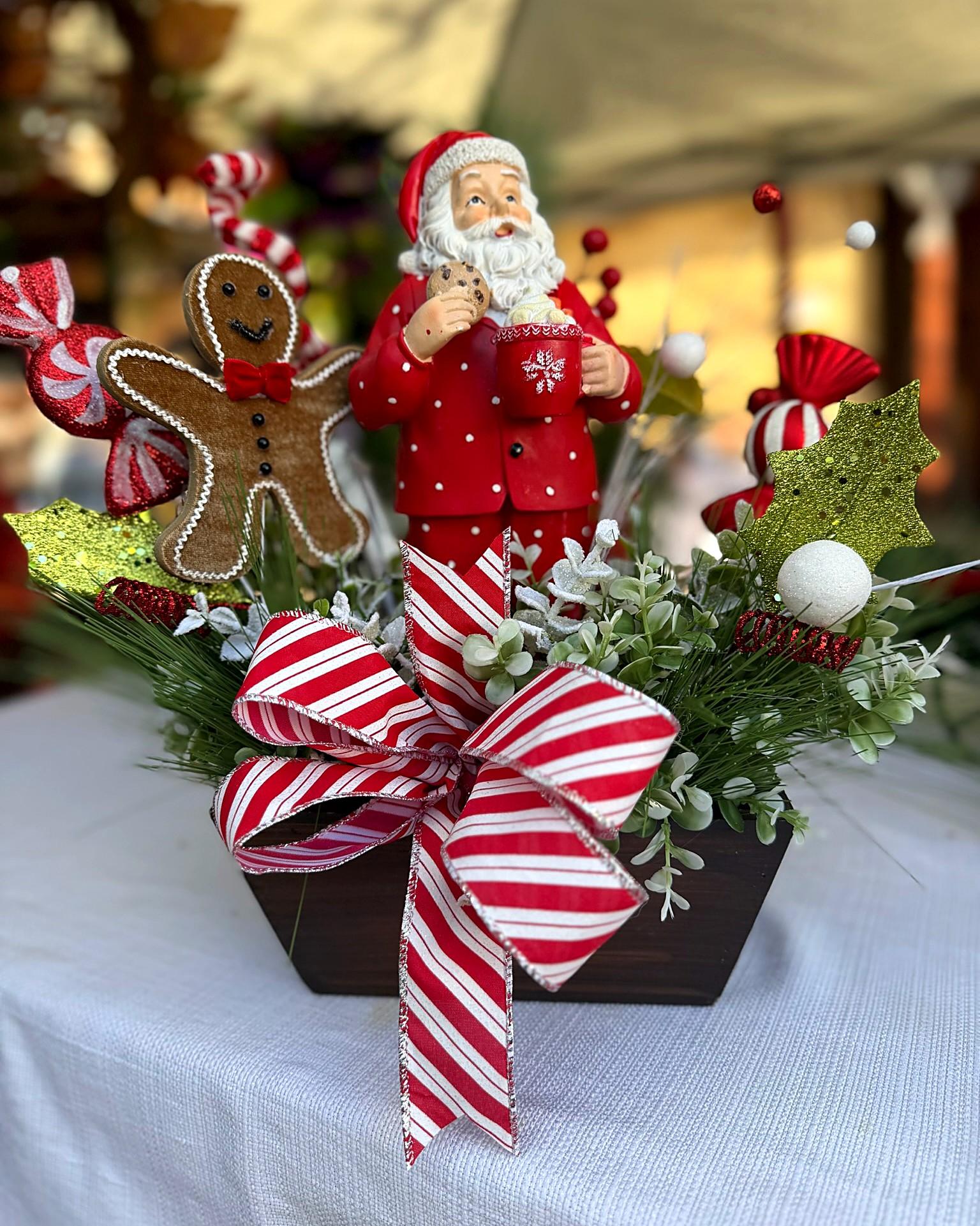 A Christmas centerpiece with a Santa figure, a gingerbread man and a red-and-white striped bow in a wooden box